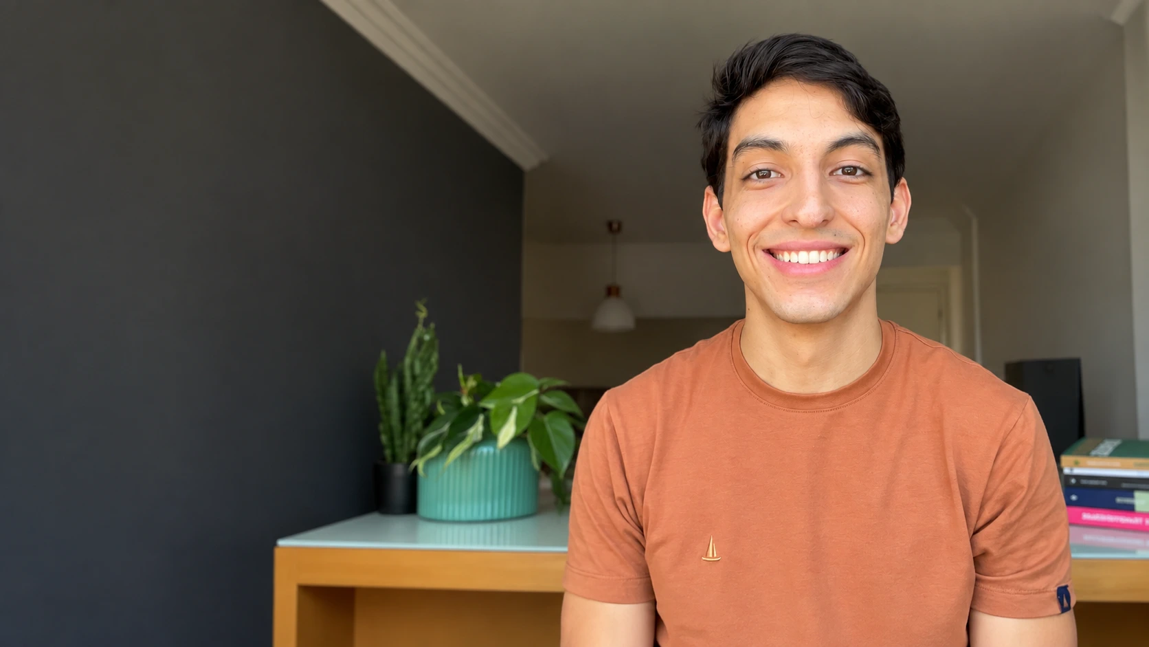 Gustavo Mota, psicólogo clínico, sorrindo, de camiseta laranja, em seu consultório